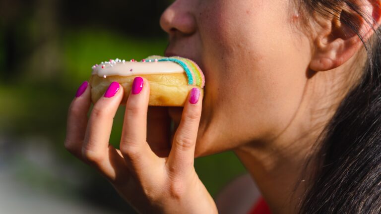 woman eating a donut, showing the relationship between sugar/diet and skin aging