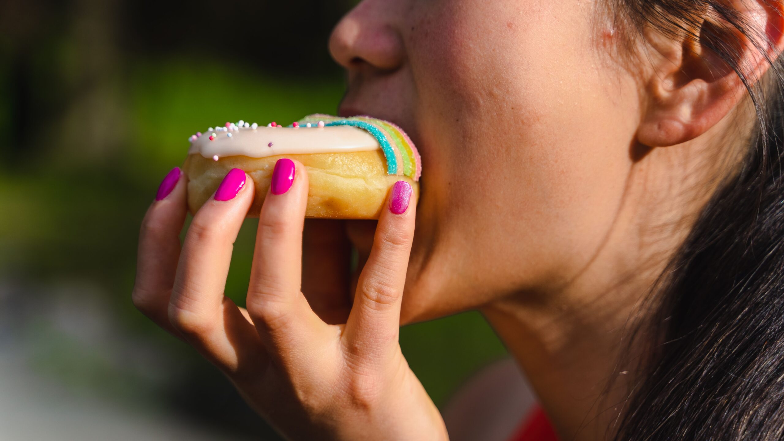woman eating a donut, showing the relationship between sugar/diet and skin aging